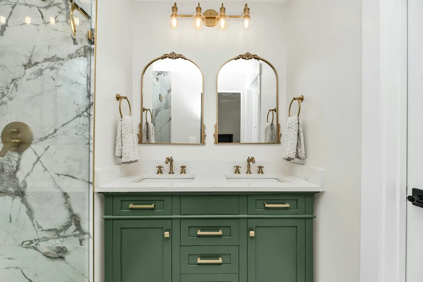 Salle de bains rénovée avec double vasque, meuble vert et carrelage effet marbre