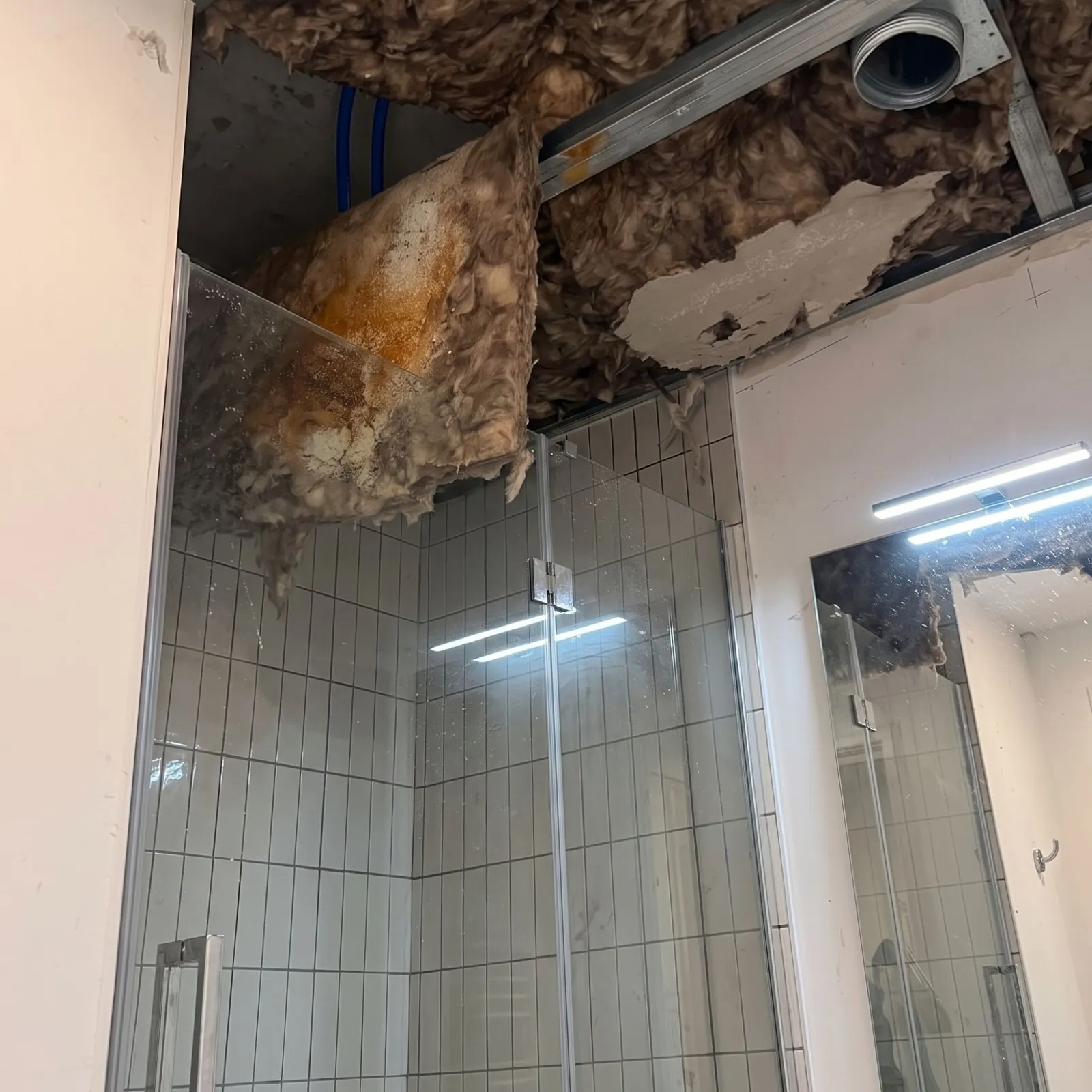 Avant : plafond effondré au-dessus de la douche après un dégât des eaux, isolant imbibé d'eau